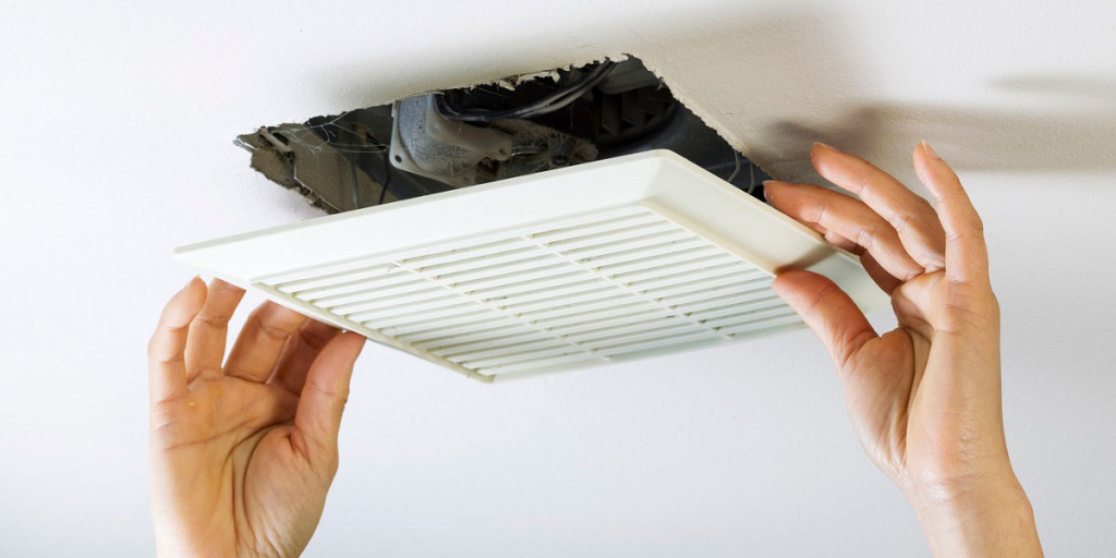 Person removing a ceiling vent cover to perform air duct cleaning.