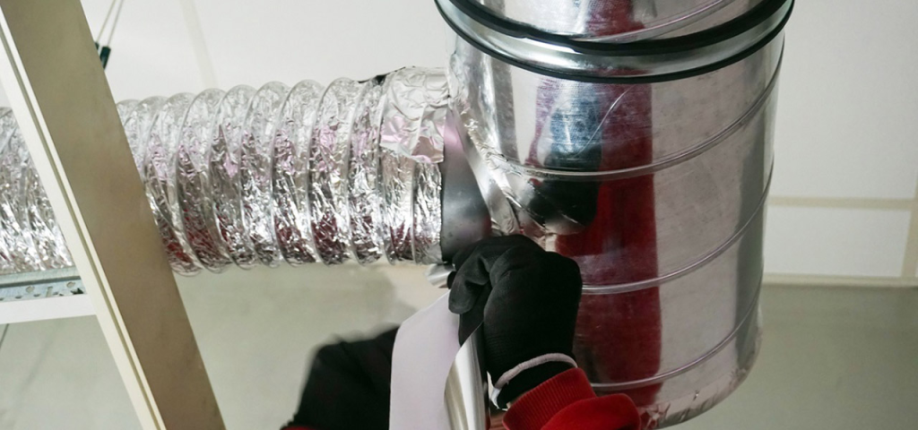 Technician sealing a flexible air duct connection during HVAC duct cleaning service.